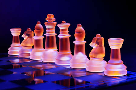 Glass chess on a chessboard lit by a colorful blue and orange light and placed on a glass chessboardの写真素材