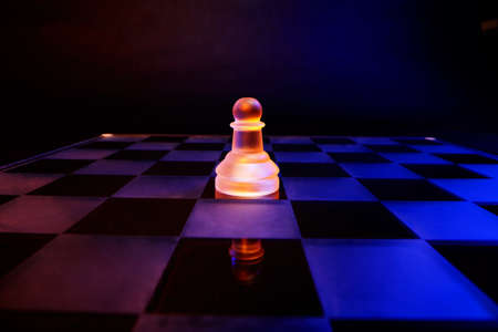 Glass chess on a chessboard lit by a colorful blue and orange light and placed on a glass chessboardの写真素材