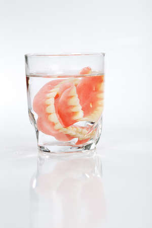 A set of dentures in a glass of water on a white backgroundの写真素材