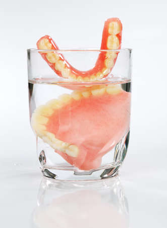 A set of dentures in a glass of water on a white backgroundの写真素材