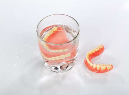 A set of dentures in a glass of water on a white backgroundの写真素材