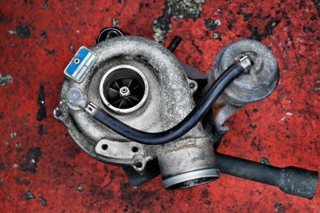 Old worn out turbocharger of a turbo diesel engine on a red backgroundの写真素材