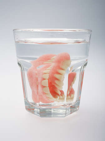 A set of dentures in a glass of water on a white backgroundの写真素材