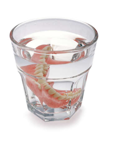 A set of dentures in a glass of water on a white backgroundの写真素材
