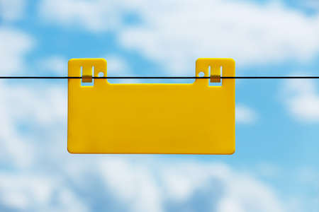 Blank yellow info plate hung on an electrical fence against blue sky with cloudsの写真素材