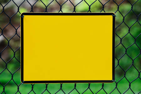 Blank yellow info plate hung on a wire fenceの写真素材