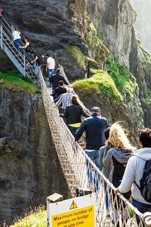 Thousands of tourists visiting Carrick-a-Rede Rope Bridge in County Antrim of Northern Ireland, hanging 30m above rocks and spanning 20m, linking mainland with the tiny island of Carrickaredeのeditorial素材