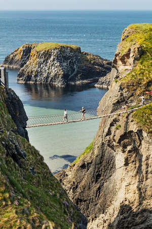 Thousands of tourists visiting Carrick-a-Rede Rope Bridge in County Antrim of Northern Ireland, hanging 30m above rocks and spanning 20m, linking mainland with the tiny island of Carrickaredeのeditorial素材