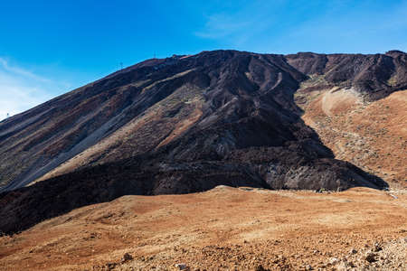 An uphill view of the colourful Teide volcano in Teide National Park, Tenerife, Canary Islands. Pictured in the distance is a cablecar leading up to the 3718 m Teide peak, the tallest peak in Spain.の写真素材