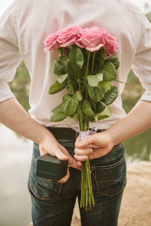 a man hiding behind a bouquet of pink roses and a ringの写真素材