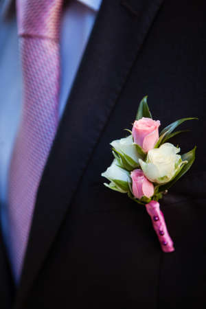 boutonniere of pink and white rosebuds on the lapel of his jacket the groom's blackの写真素材