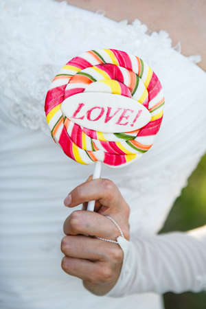 bride in a white dress and gloves holding a candy on a stick with an inscription loveの写真素材