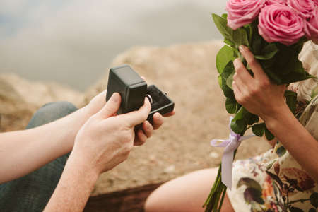 a man gives a woman a box with a diamond ring in the park