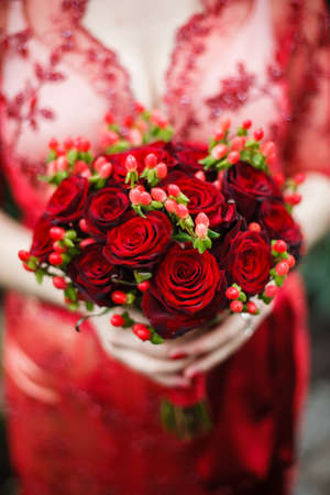 bride red lace dress is holding a round bouquet of red rosesの写真素材