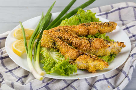 fried fish with lettuce and lemon on a light wooden tableの写真素材