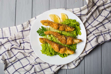 fried fish with lettuce and lemon on a light wooden tableの写真素材