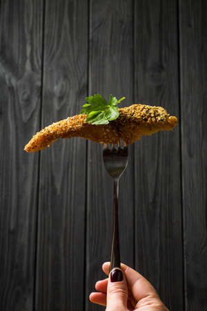 Pieces of fried Fish on a fork on a dark wooden background