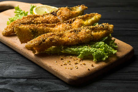 fried fish on a wooden board with lettuce