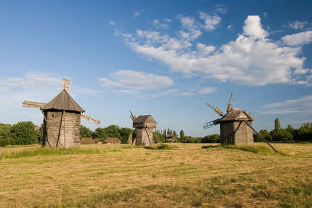 two old wooden windmills with a broken roof on a green field