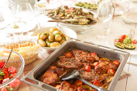 Baked meat with tomatoes and potatoes on a baking sheet, serving tableの写真素材