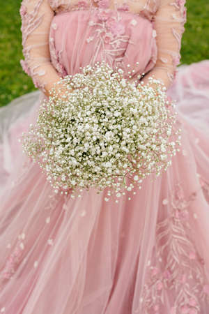 The bride in a pink dress is holding a bouquet of gypsophilaの写真素材