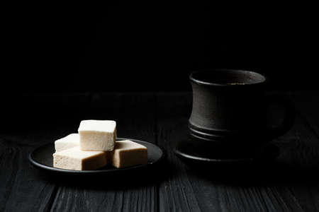 White marshmallow on a black plate on black wooden table with a cup of coffe
