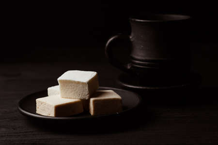 White marshmallow on a black plate on black wooden table with a cup of coffeの写真素材