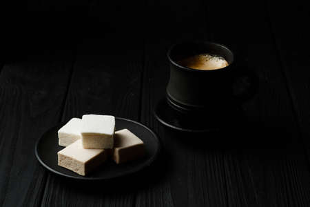 White marshmallow on a black plate on black wooden table with a cup of coffe