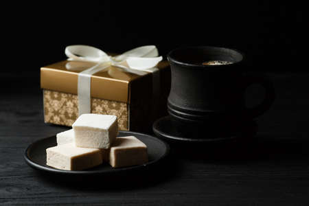 White marshmallow on a black table with a cup of coffe and golden gift boxの写真素材