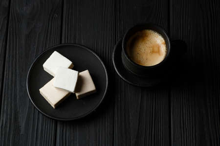 White marshmallow on a black plate on black wooden table with a cup of coffeの写真素材