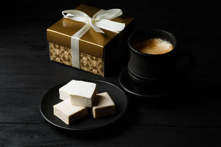 White marshmallow on a black table with a cup of coffe and golden gift boxの写真素材