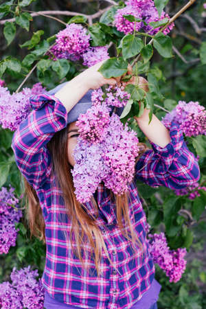 Photo of young model girl in colorful shirt hiding her face in summer lilac gardenの写真素材