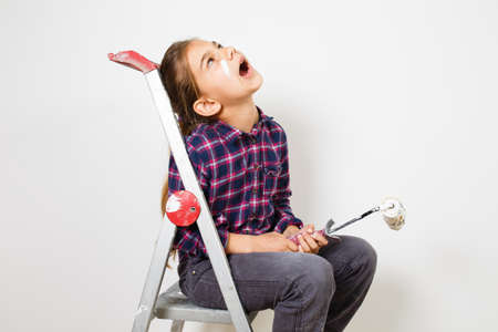 Teen girl painter using a brush on white wall in house. Repair at homeの写真素材