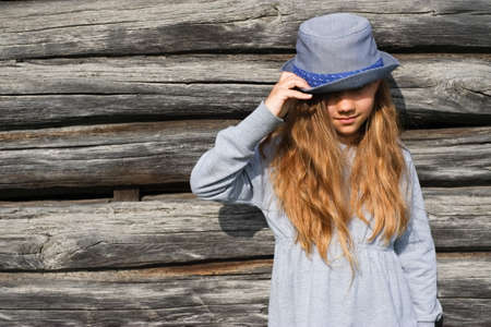Joyful teen girl in casual clothes and blue hat posing by a wooden wall. Active lifestyle. Youth fashionの写真素材