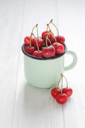 cherry in tea cup on a white wooden table close upの写真素材