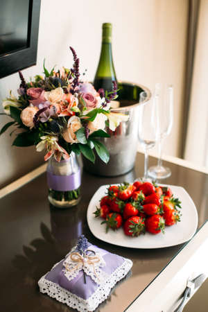 A wedding bouquet, a boutonniere, a bottle of champagne are on the table in the bride's room.の写真素材