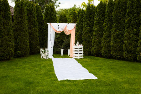 Wedding arch decorated with cloth outdoors. Beautiful wedding set up. Wedding ceremony on green lawn in the garden. Part of the festive decor.の写真素材