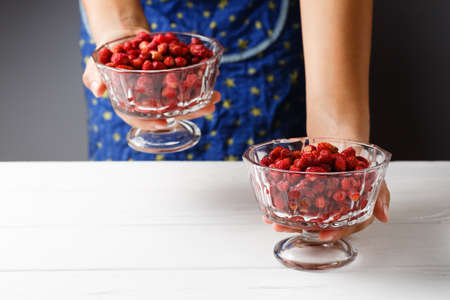 A girl holds a glass bowl with ripe red strawberries in his hands
