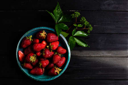 Contrast photo: strawberries in a green plate on a black tableの写真素材