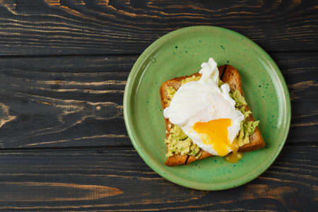 Wholemeal bread toast and poached egg with avocado on green plate on wooden tableの写真素材