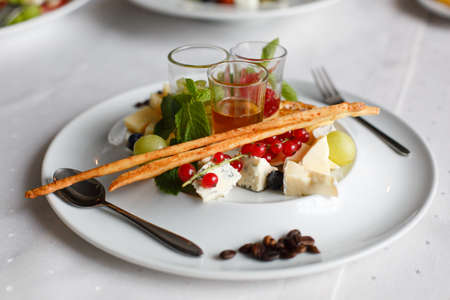 Plate with brie cheese, parmesan, grapes, currants and sauces on the festive table