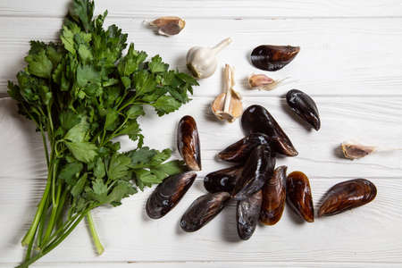 Cook ingredients - fresh raw mussels with parsley and garlic on white wood background