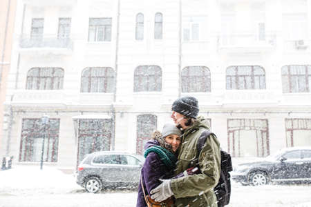 Happy young couple in winter snowy day having fun at city backgroundの写真素材