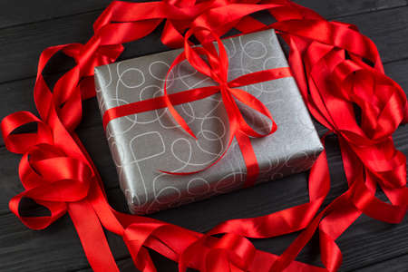 Grey silver gift box with red ribbon bow on black wooden table. Boxing dayの写真素材