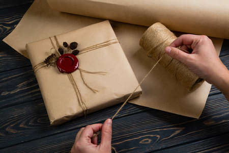 Process of package gift wrapped in craft paper with string and glued wax seal on wooden black...