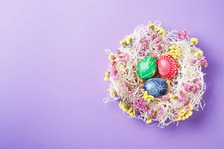 Hand painted different colors easter eggs in nest and flowers on violet paper backgroundの写真素材