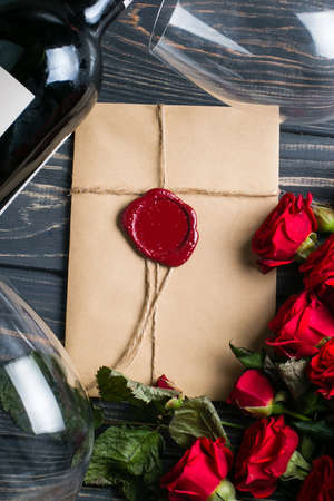 Bottle of wine, glasses, envelope with wax seal and red rose flowers on wooden tableの写真素材