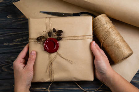 Process of package gift wrapped in craft paper with string and glued wax seal on wooden black backgroundの写真素材