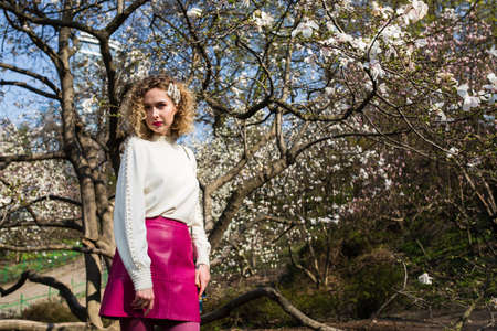 Portrait of beautiful girl with curly long hair in white blouse walks in garden of white magnolia