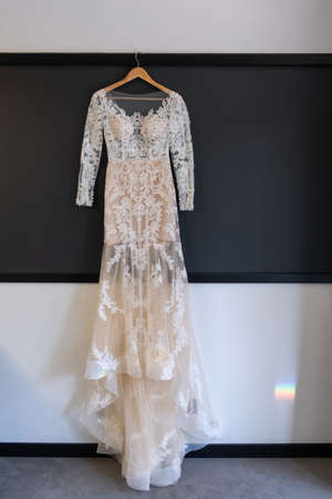 Bright beige wedding dress hanging on a hanger near a windowの写真素材